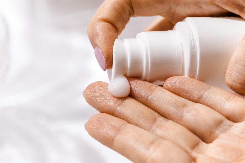 An image featuring a woman's hands gently applying moisturizer, emphasizing the importance of skincare and self-care routines for maintaining healthy and hydrated skin.