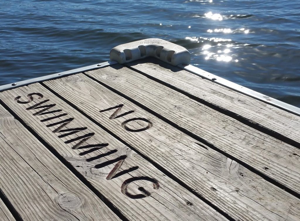 An image of a pier extending into a lake, with the words 'no swimming' carved into its surface, serving as a clear indication of the prohibition or restriction on swimming in that area.