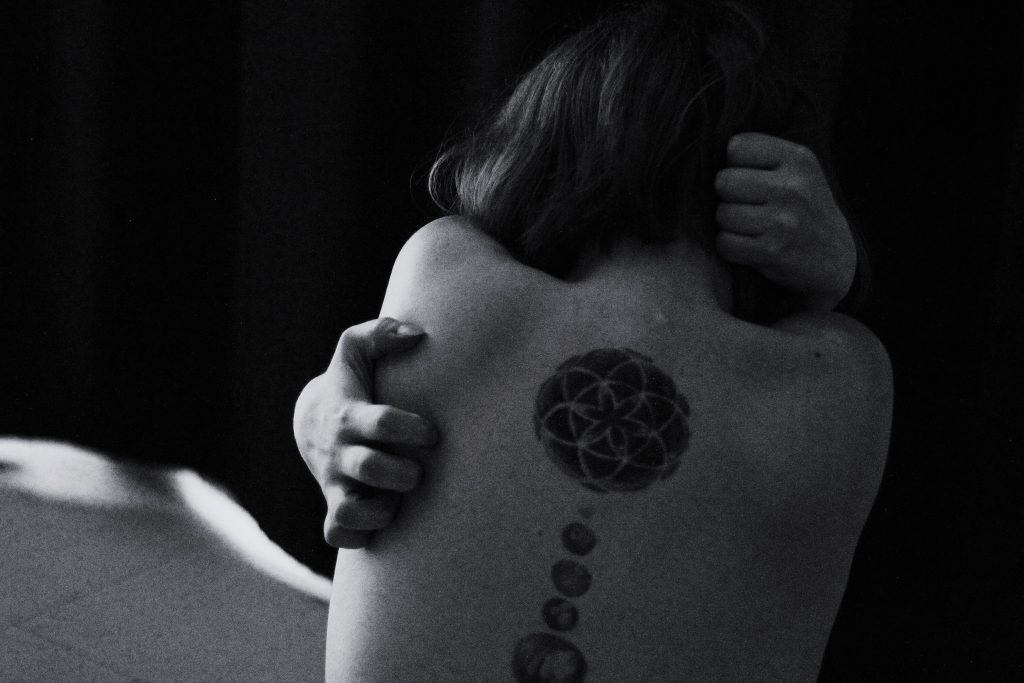 An image of a woman with a tattoo on her back, reaching with her hand to scratch it, demonstrating the desire for relief or comfort from an itch or irritation on her tattooed skin.