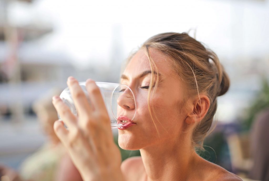 An image of a woman holding a glass and drinking water, demonstrating the importance of hydration and maintaining a healthy lifestyle through proper water consumption.